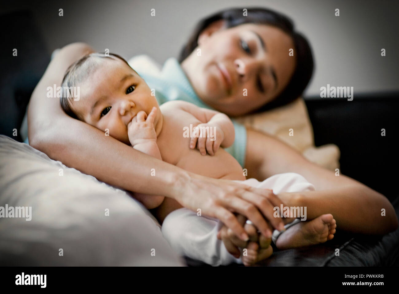 Young baby being held by it's mother on a sofa. Stock Photo