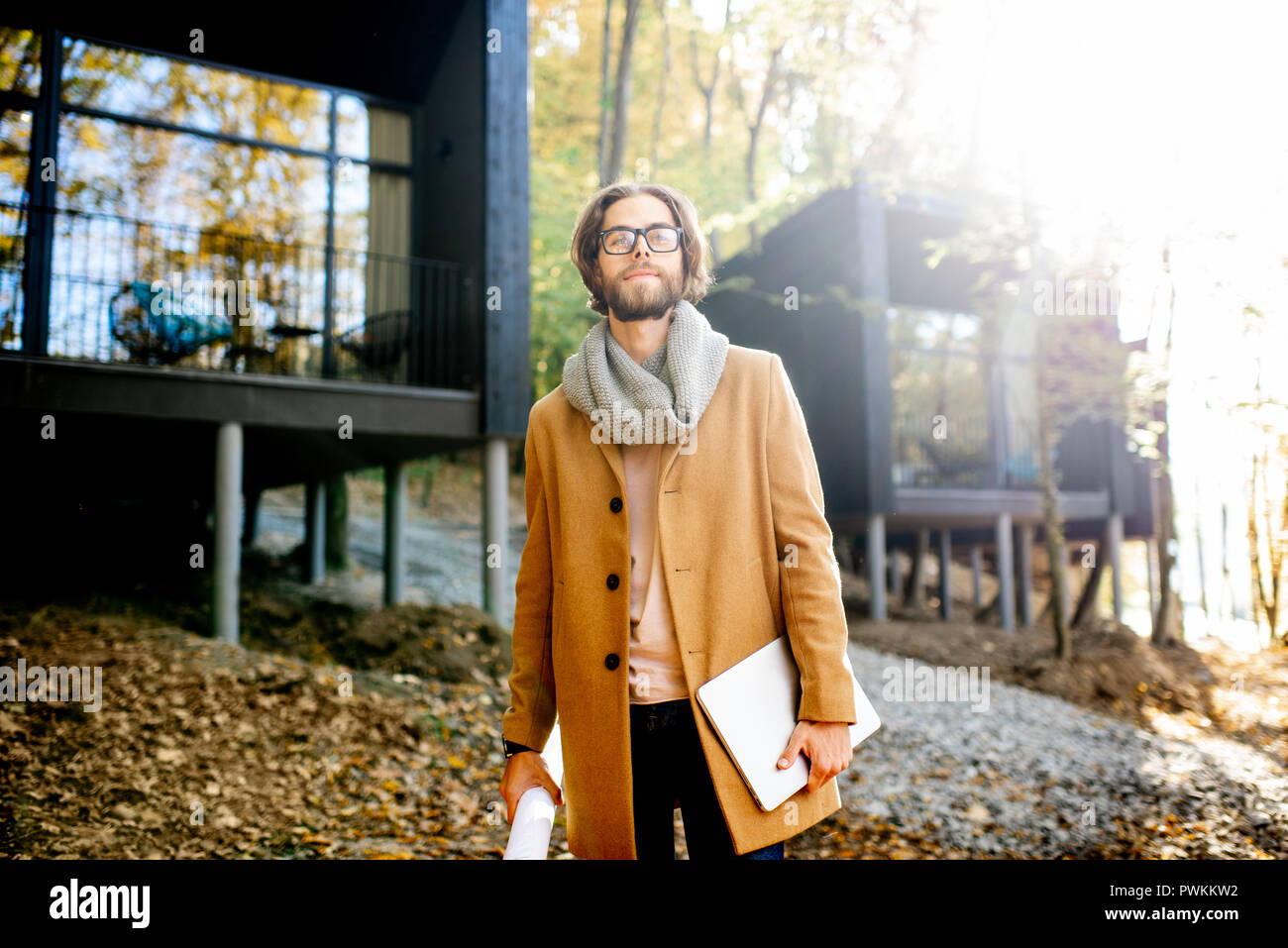 Portrait of a handsome man architect standing with laptop in front of the modern houses in the forest Stock Photo
