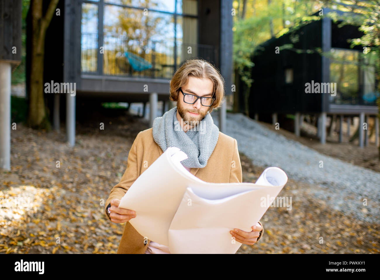 Portrait of a handsome man architect standing with drawings in front of the modern houses in the forest Stock Photo