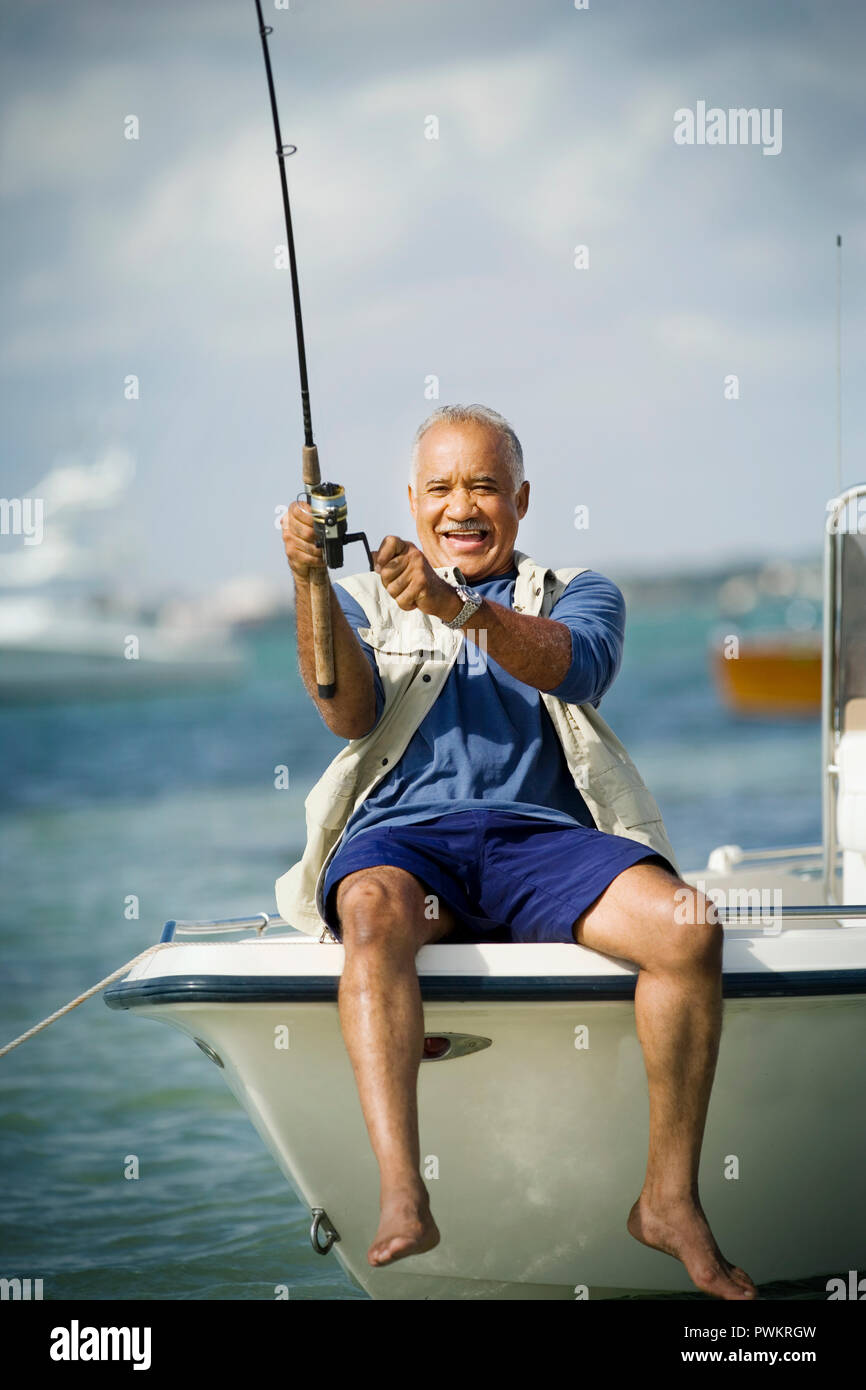 Smiling mature man fishing off the side of a boat in the ocean. Stock Photo