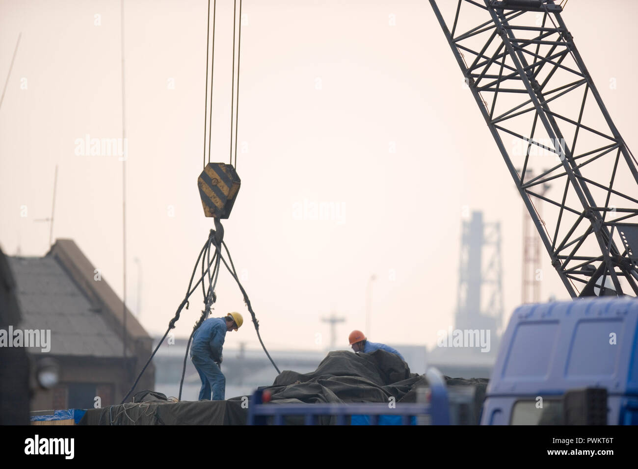 Two male construction workers hooking cables to a crane in a shipping yard. Stock Photo