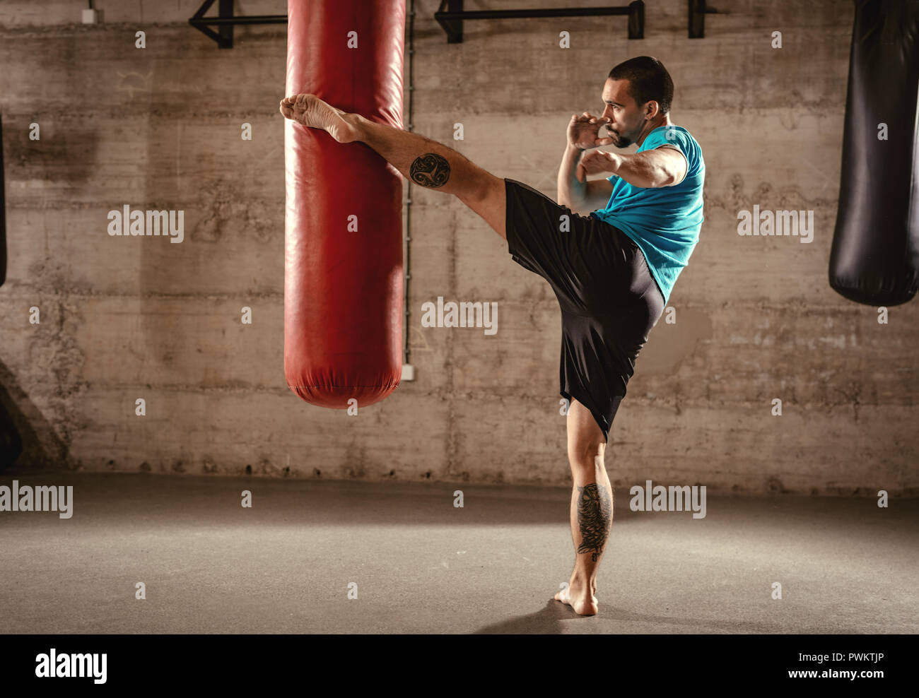 Muscular man punching with leg a boxing bag on cross fit training at the  gym Stock Photo - Alamy