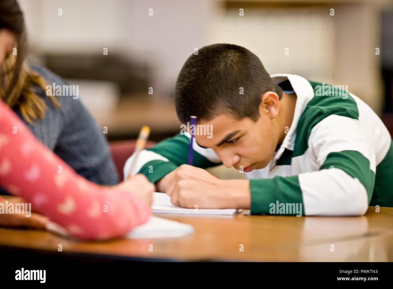 Teenage boy doing schoolwork while seated at a desk. Stock Photo