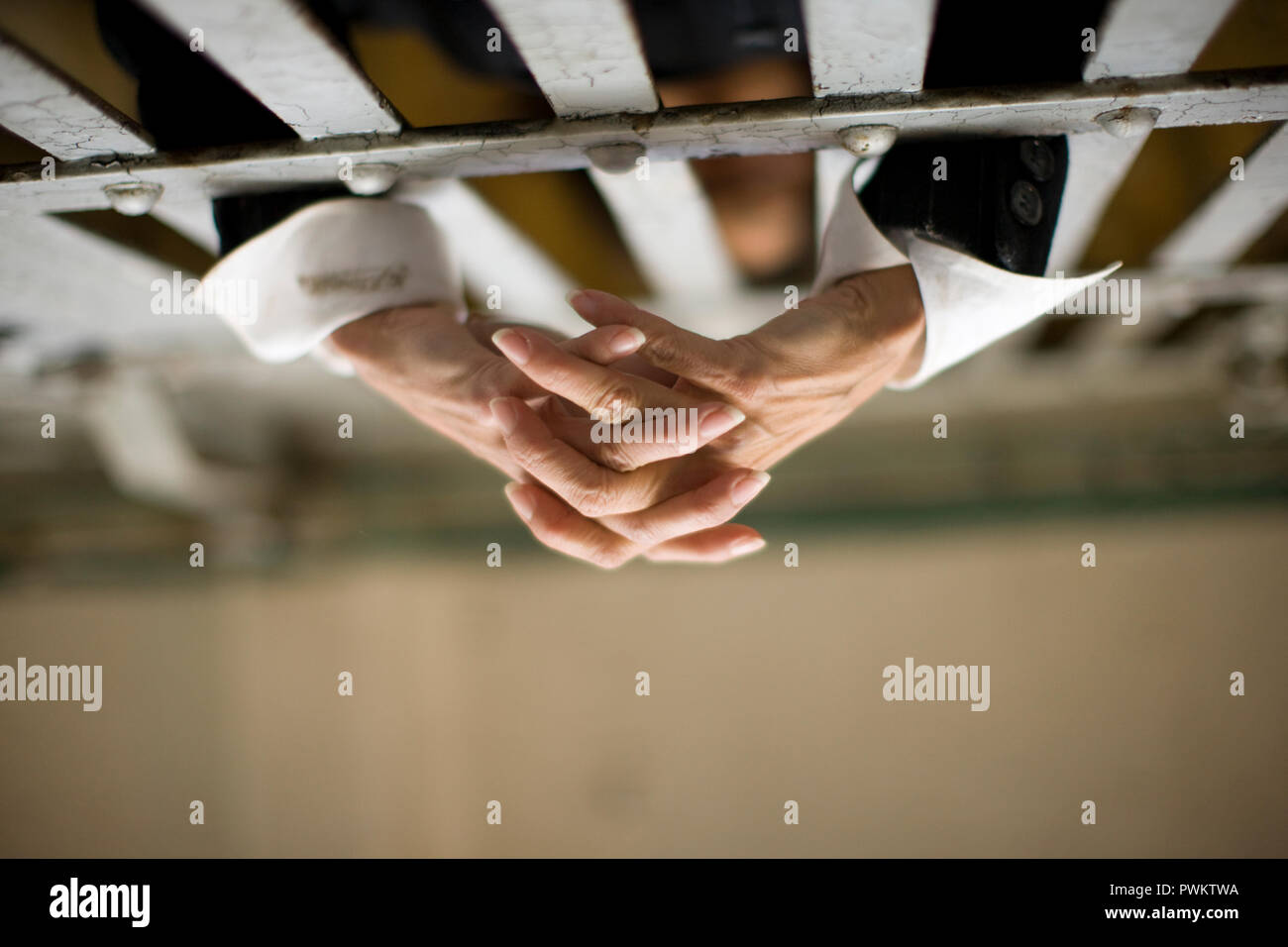 Hands of a mid-adult woman through bars of a prison cell in a derelict building. Stock Photo