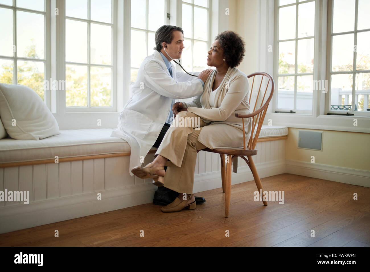 Middle aged doctor listening to a mature patient's heartbeat with a stethoscope. Stock Photo