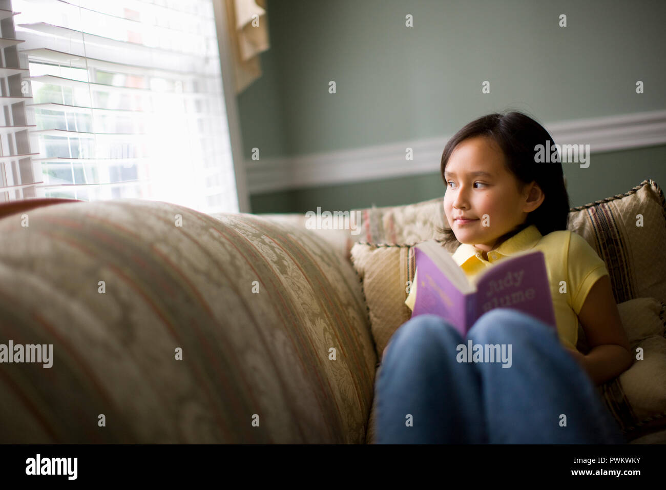 Young girl reading a book in her living room. Stock Photo