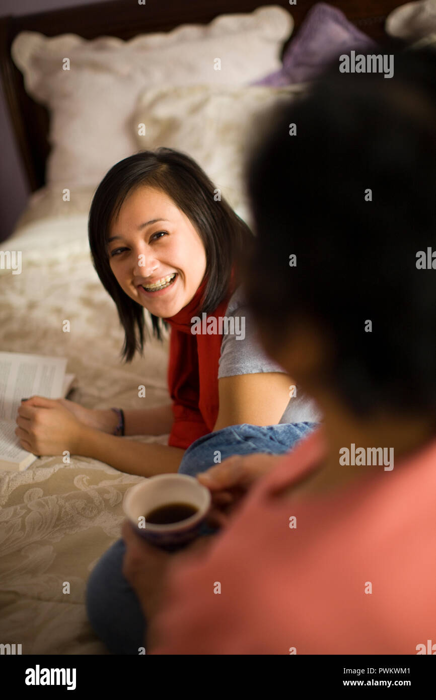 Teenage girl reading in her bedroom and talking to her mom Stock Photo
