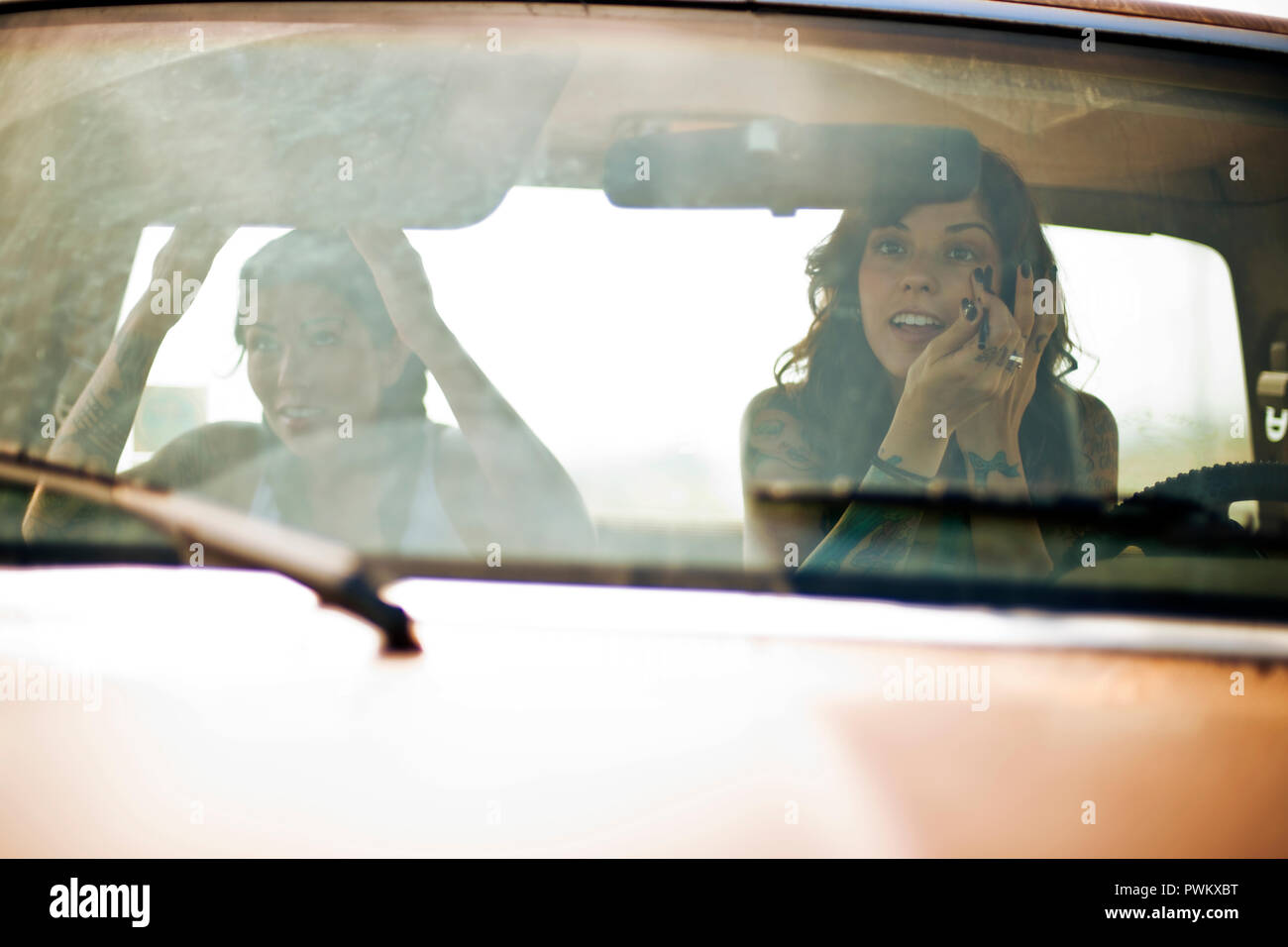 Two female friends sitting in a pick-up truck, applying makeup in the rear view mirror. Stock Photo