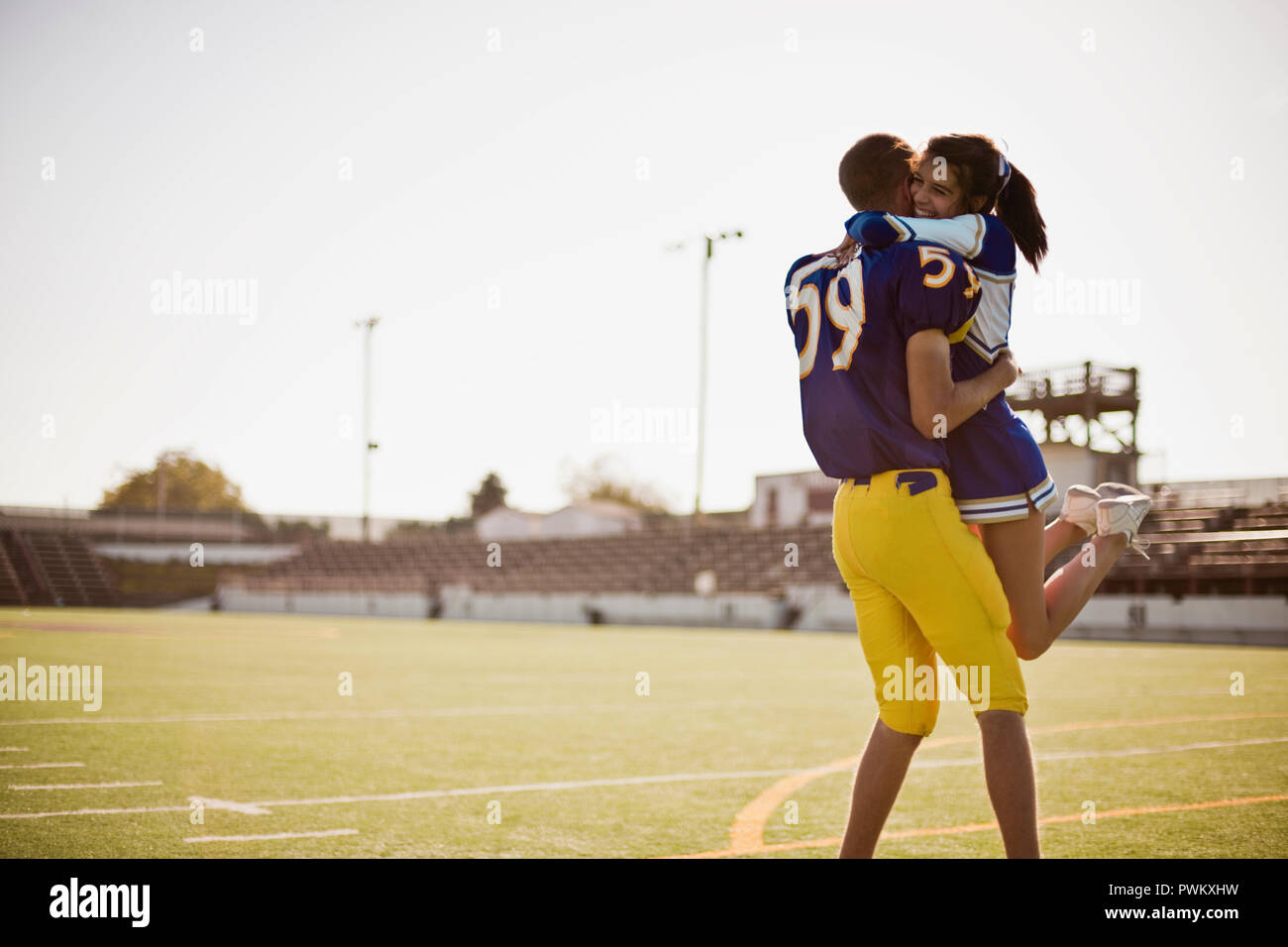 Football player picking up cheerleader in a lover's embrace. Stock Photo