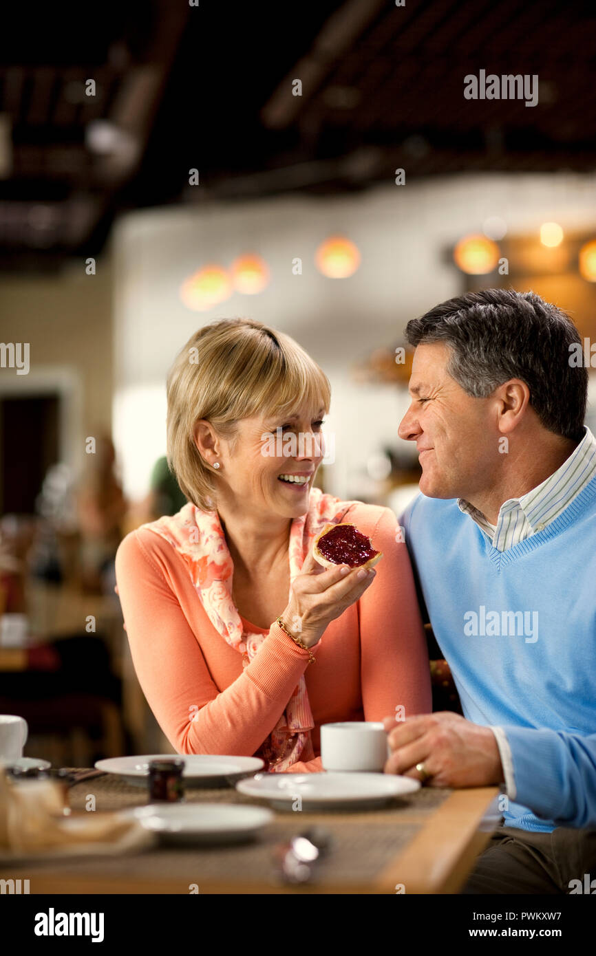 Affectionate mature couple enjoy eating breakfast together at a cafe. Stock Photo