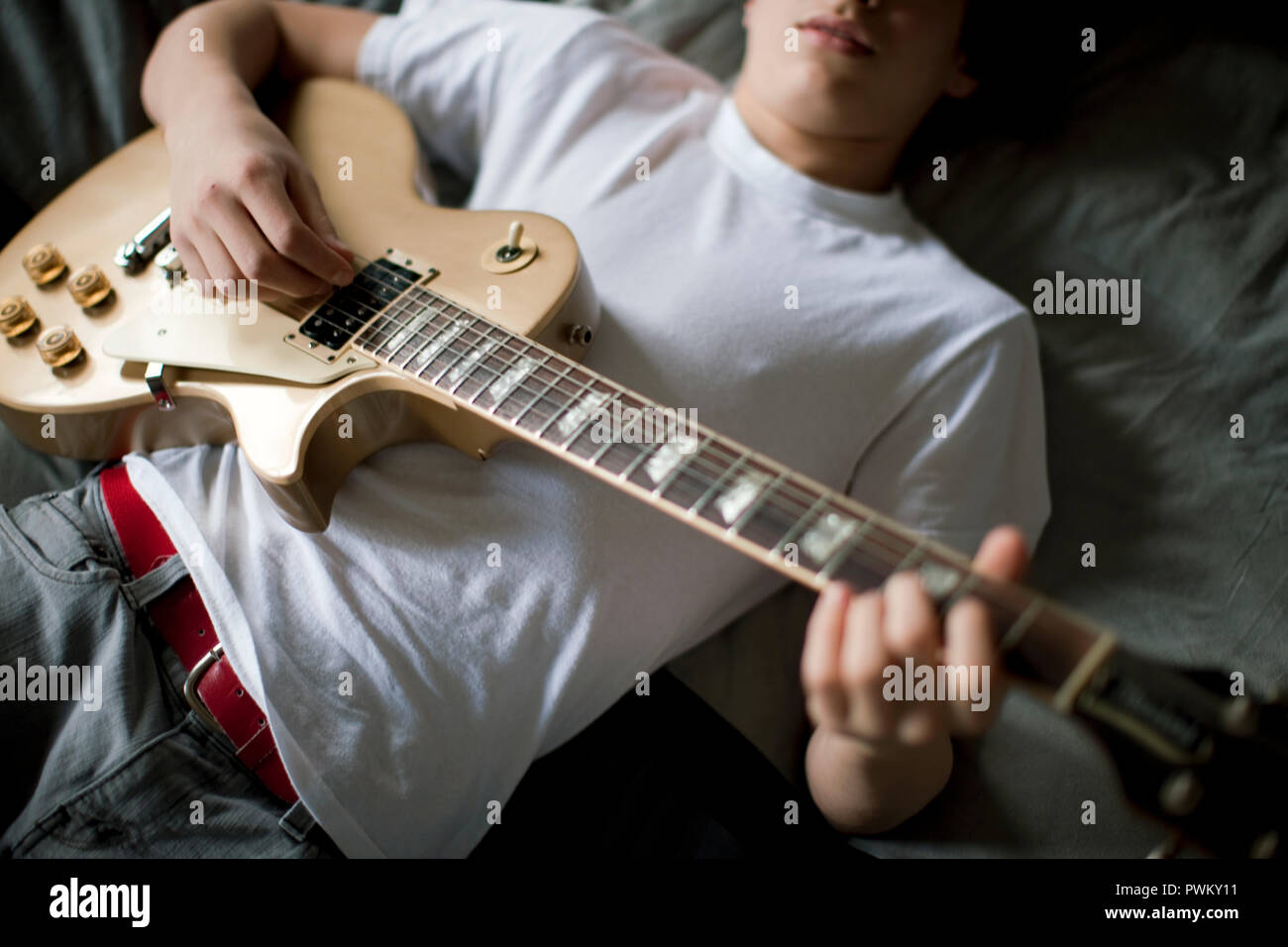 Boy lying on bed playing guitar. Stock Photo