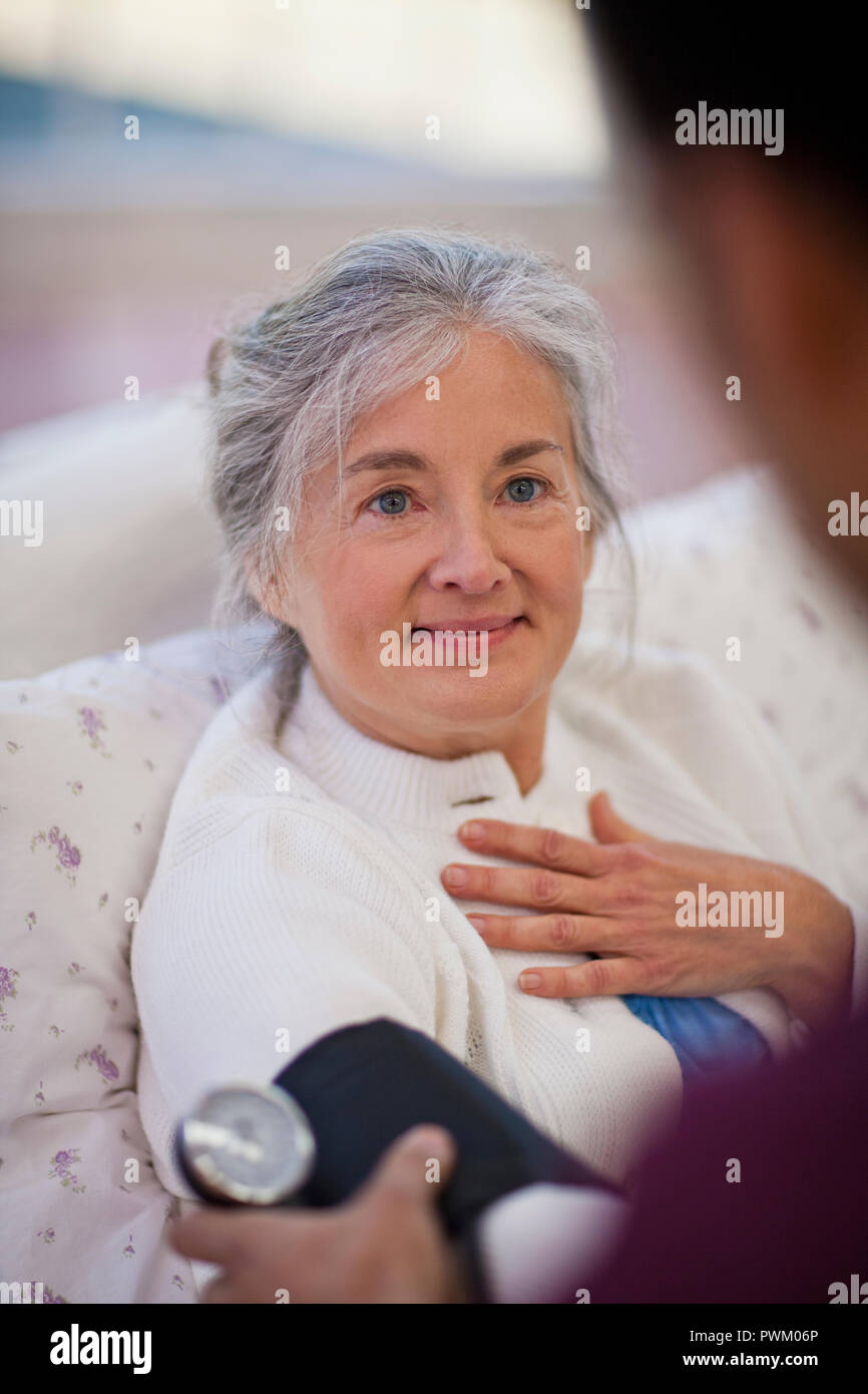 Hopeful senior woman looking at a male nurse while having her blood pressure taken. Stock Photo
