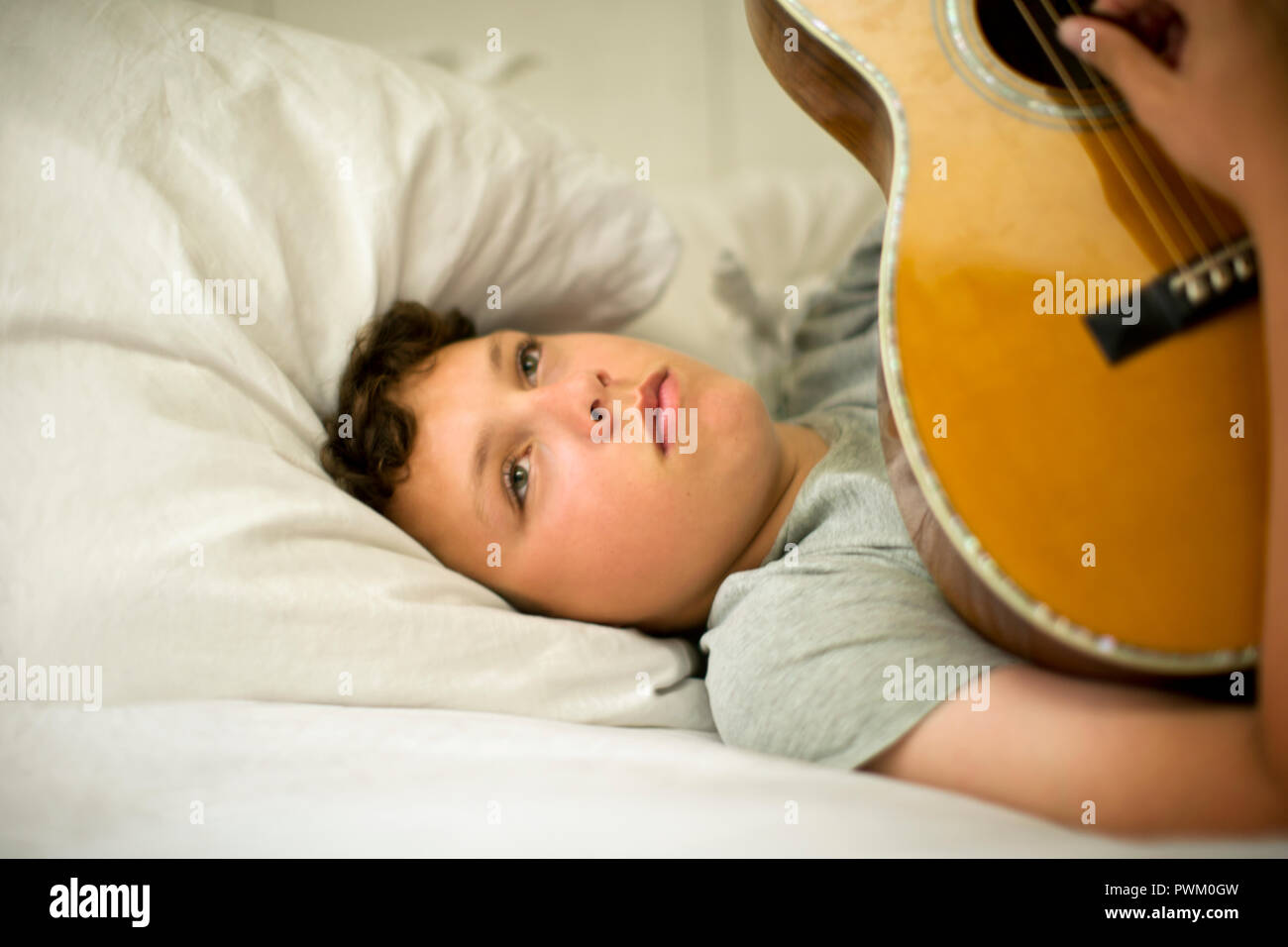 Teenage boy lying on his bed playing an acoustic guitar. Stock Photo