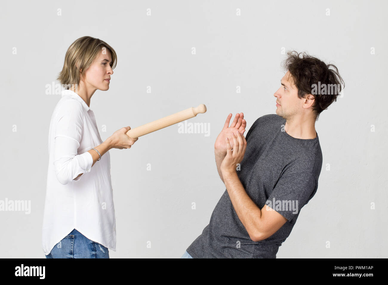 Young couple arguing in kitchen. Frustrated wife with rolling pin