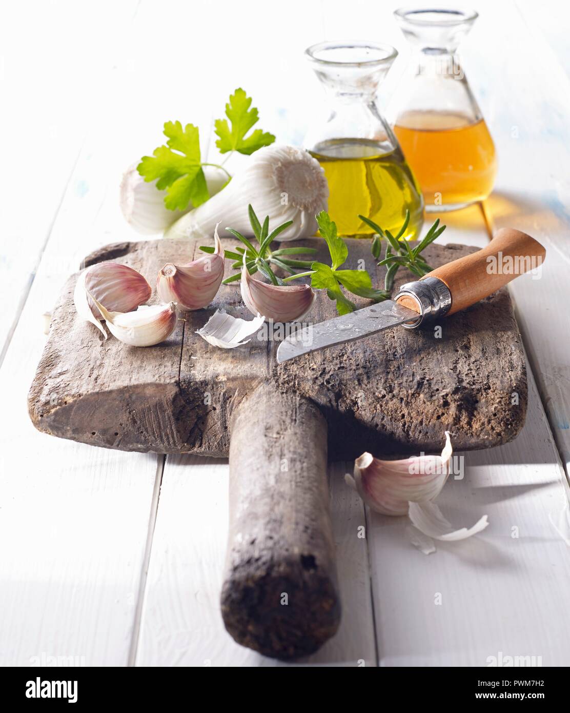 Cloves of garlic with oil, vinegar and a knife on an old wooden board Stock Photo