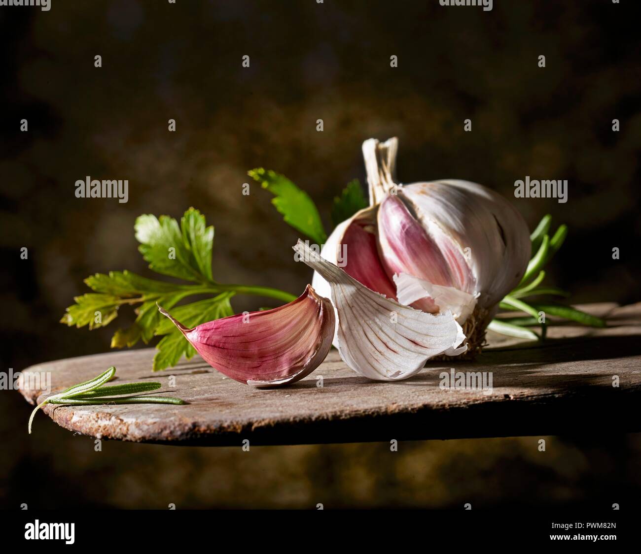 A garlic bulb and flat-leaf parsley on a wooden board Stock Photo