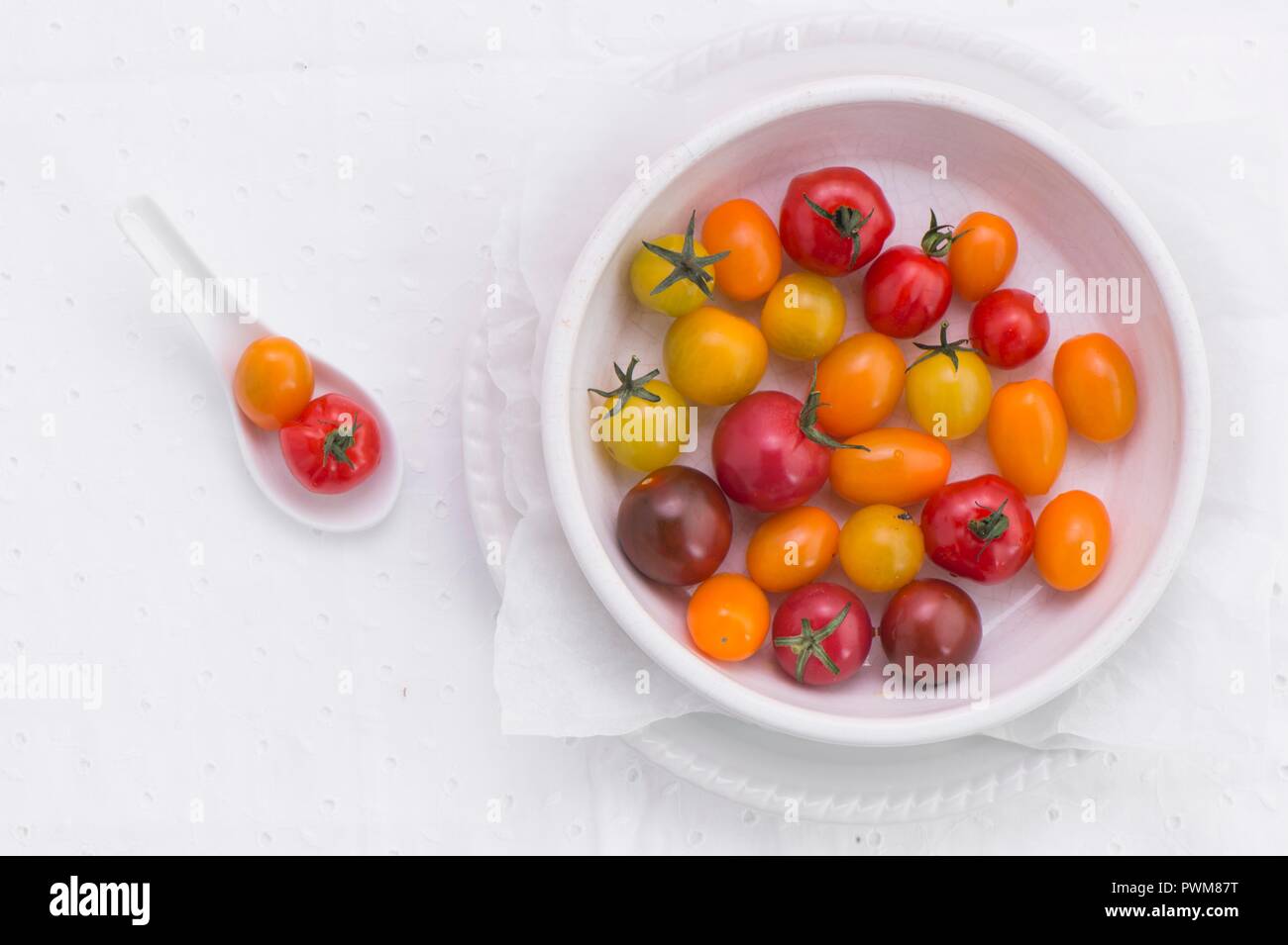 Various different coloured tomatoes in a porcelain bowl and on a spoon (seen from above) Stock Photo