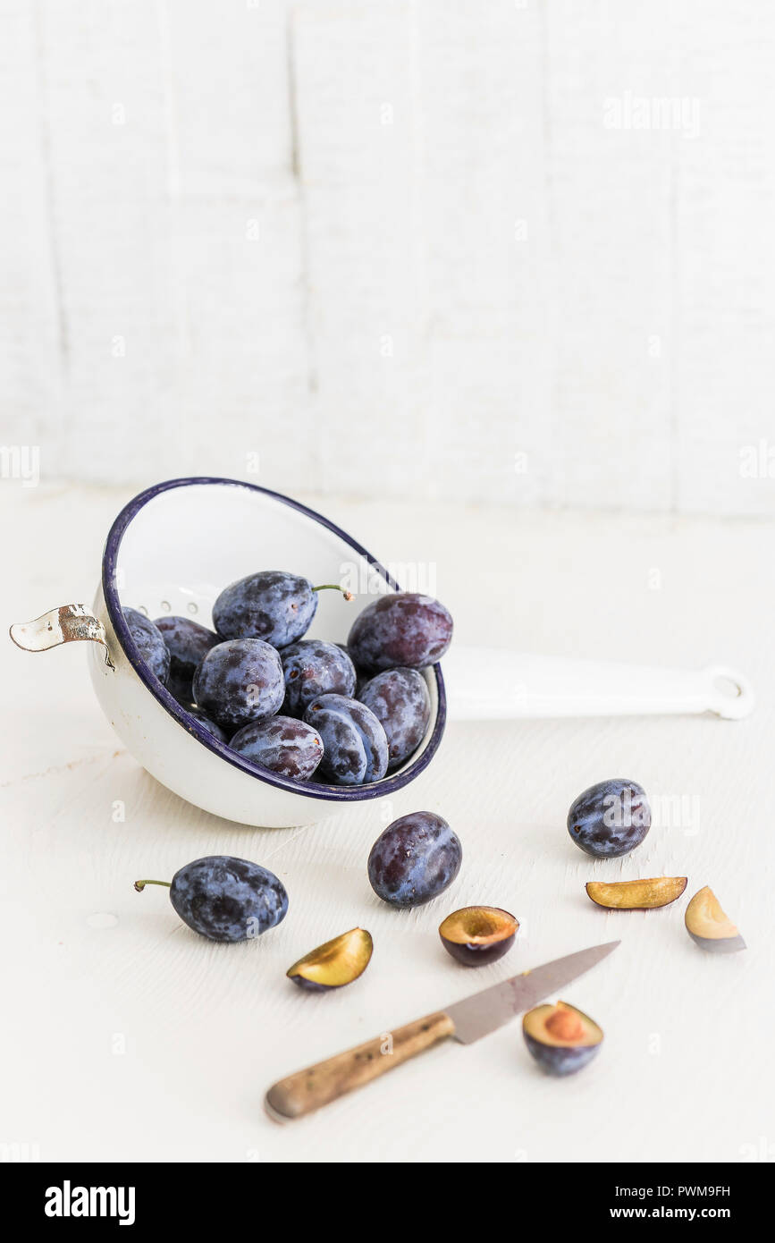 Damsons in a colander with a knife on a light surface Stock Photo