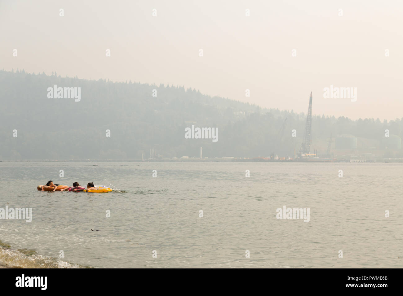 VANCOUVER, BC, CANADA - AUG 20, 2018: Children play in the ocean near a North Vancouver beach with the haze from forest fires obscurring the view. Stock Photo