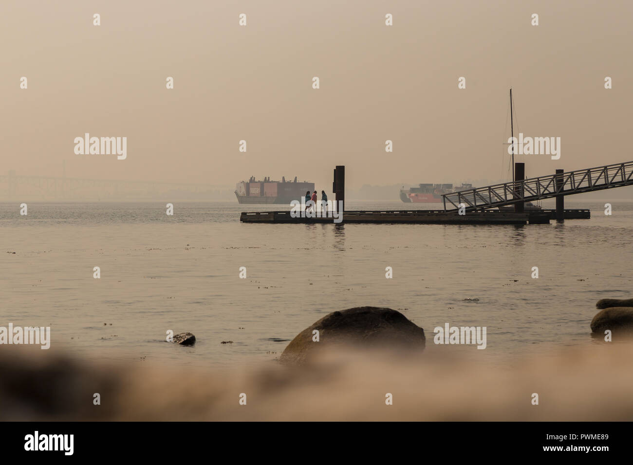 VANCOUVER, BC, CANADA - AUG 20, 2018: Children play on a dock near the ocean near a North Vancouver beach with the haze from forest fires obscurring the view. Stock Photo