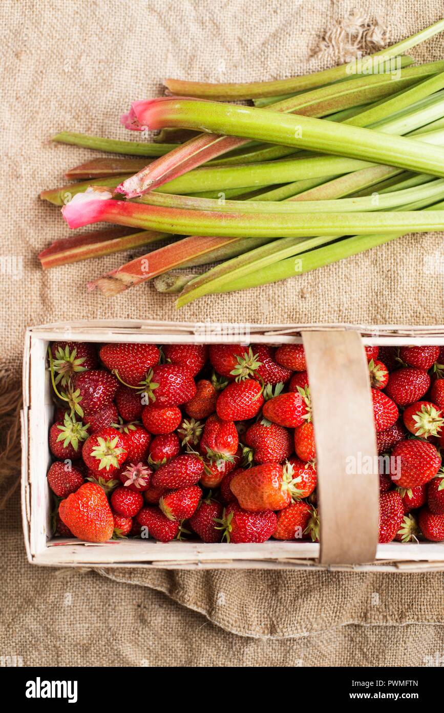 Strawberries in a wooden basket next to rhubarb Stock Photo
