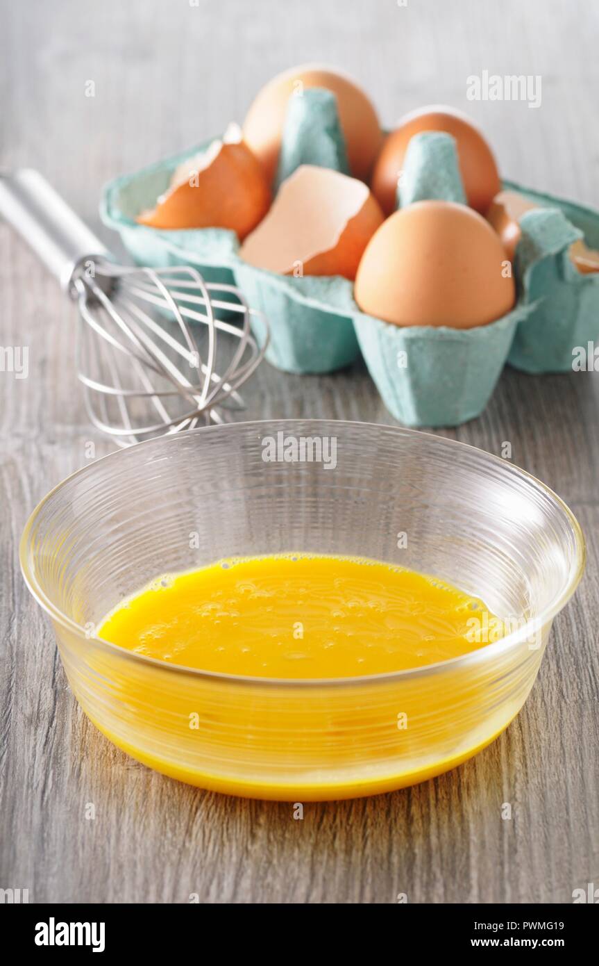 Egg yolks in a bowl, eggs in an egg box and a whisk Stock Photo