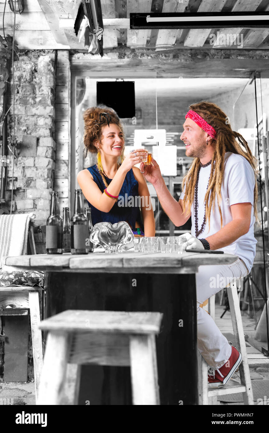 Two stylish beaming flower children chilling while drinking alcohol in pub Stock Photo
