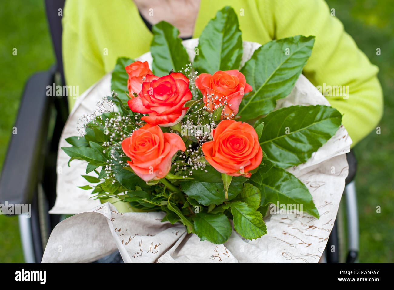 Disabled elderly woman sitting in wheelchair, receiving a flower
