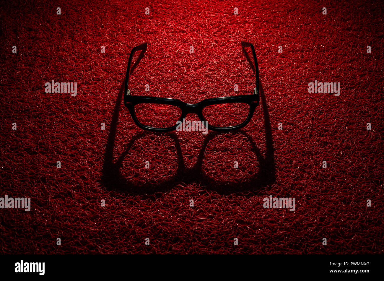 Studio shot of a black, full rim, rectangular, spectacle frame with direction lighting producing a hard front shadow on red textured background. Stock Photo