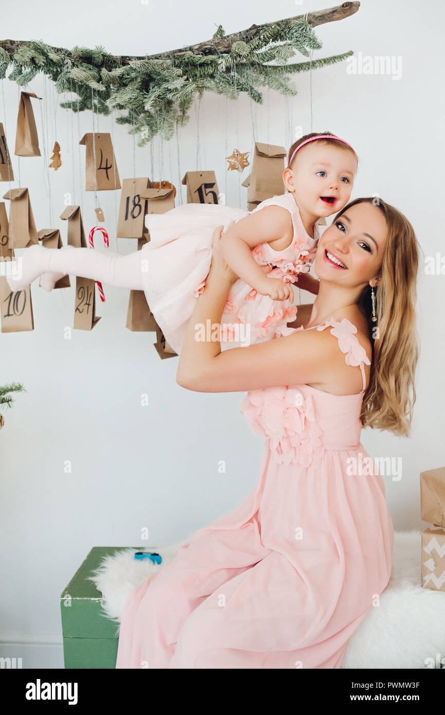 https://c8.alamy.com/comp/PWMW3F/beautiful-and-positive-blonde-mom-holding-cute-little-daughter-by-hands-rising-up-posing-near-christmas-decoration-mother-with-baby-in-pink-dresses-PWMW3F.jpg