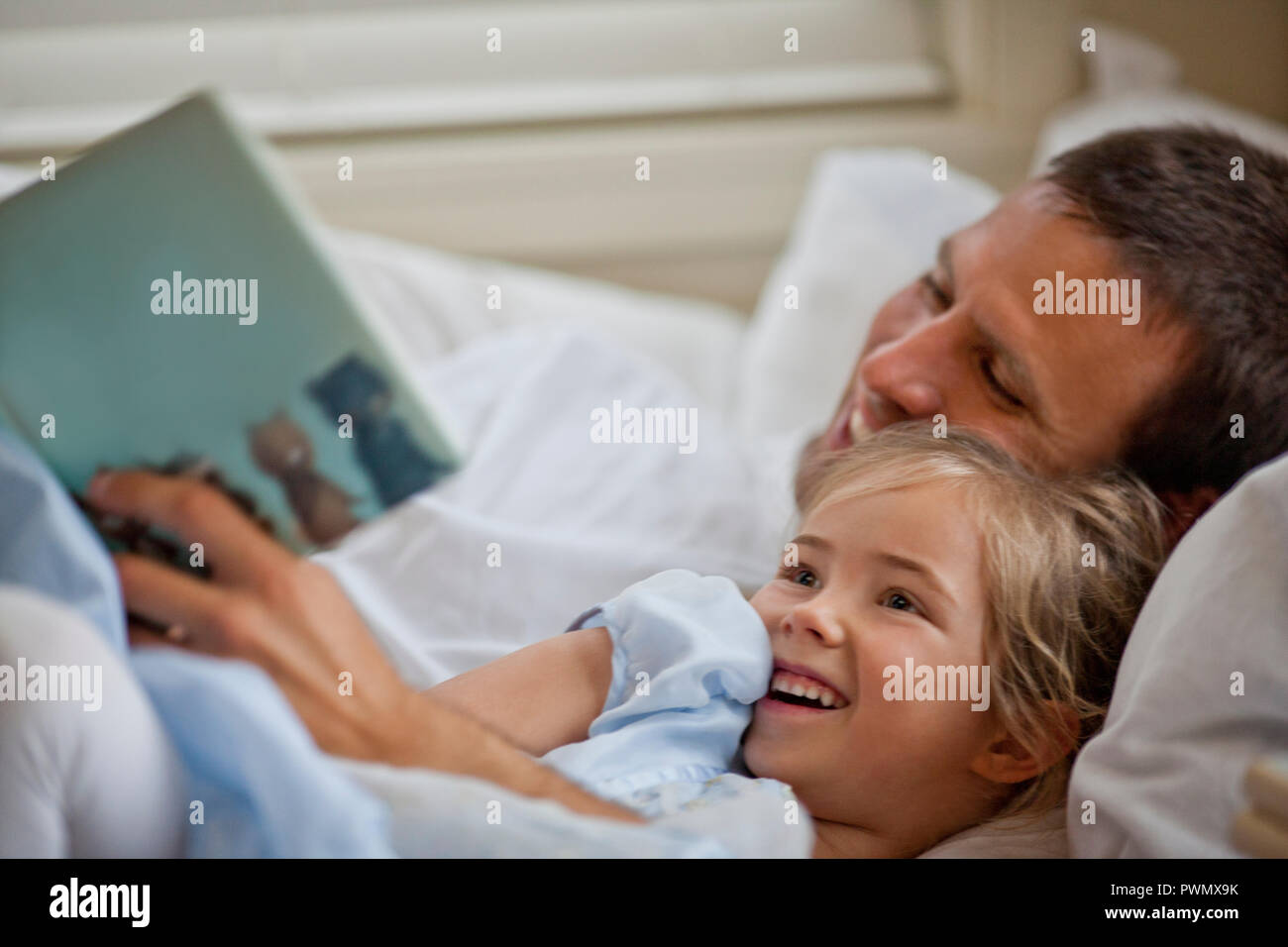 Happy father lying down reading a book with his daughter. Stock Photo