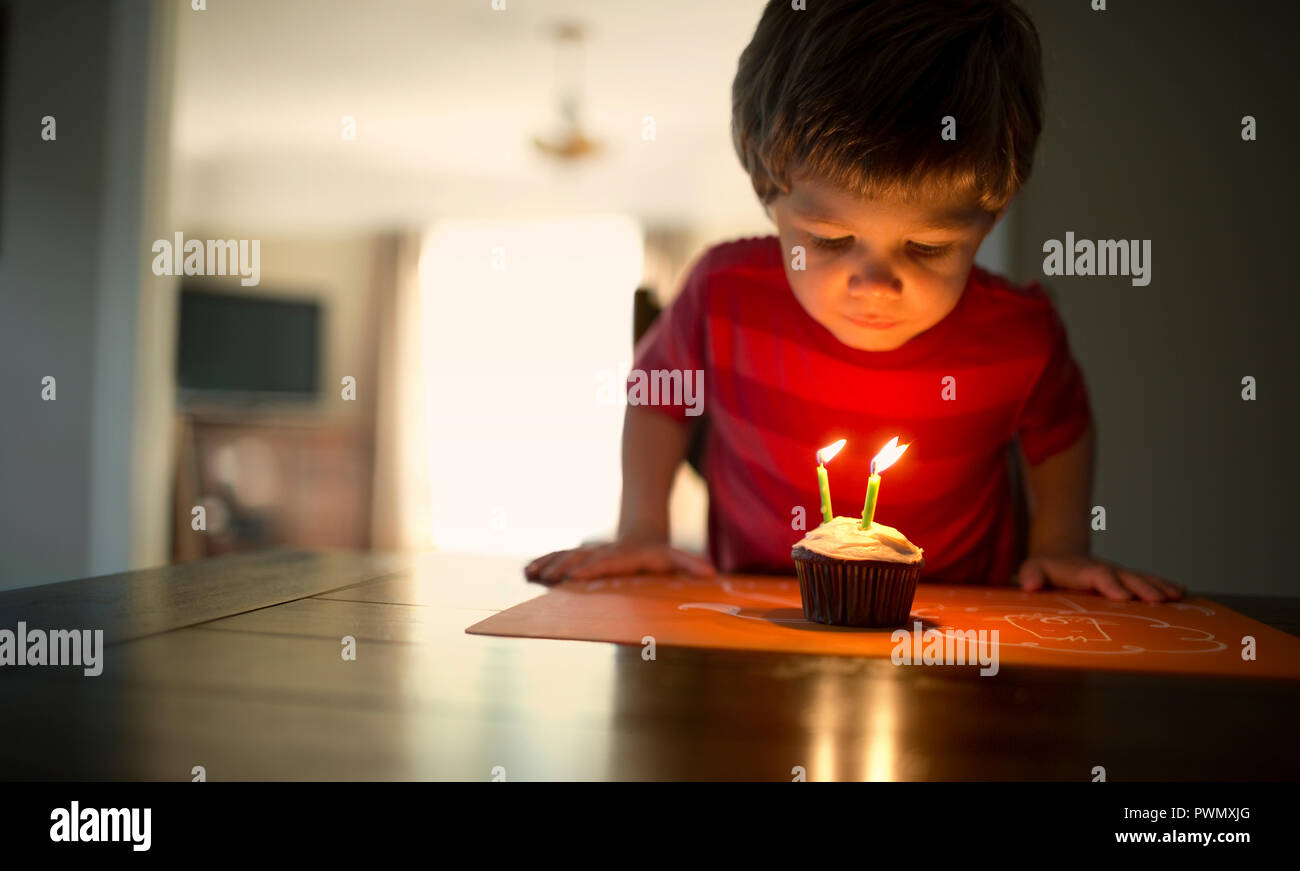 Young boy blowing out three candles on his birthday cupcake. Stock Photo