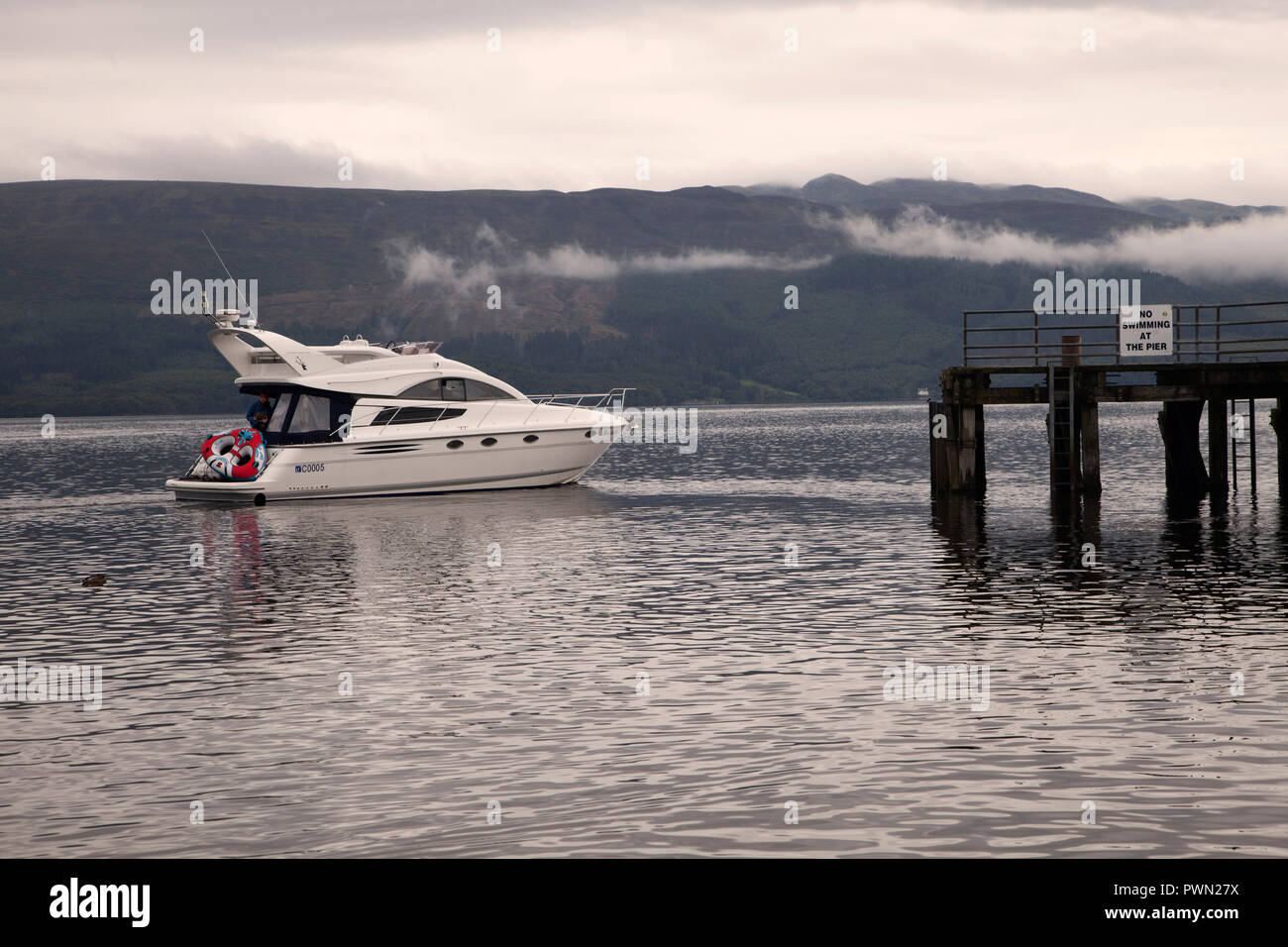 Motor cruiser approaching Luss pier on Loch Lomond in early morning with mist on the hills beyond. Stock Photo