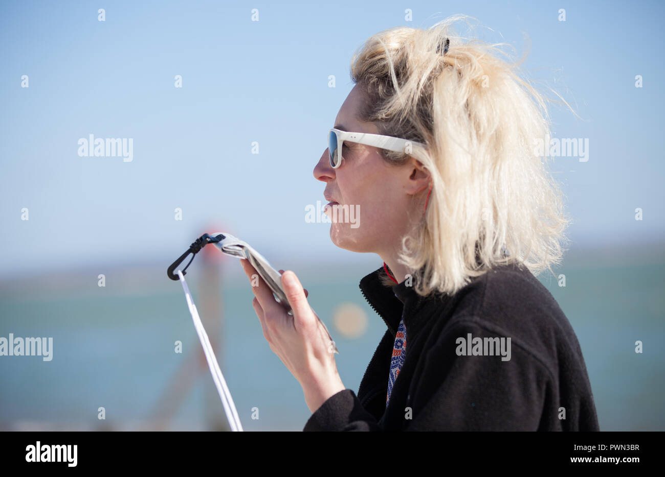 Woman on mobile phone, on speaker, by the seaside with water proof case on Stock Photo