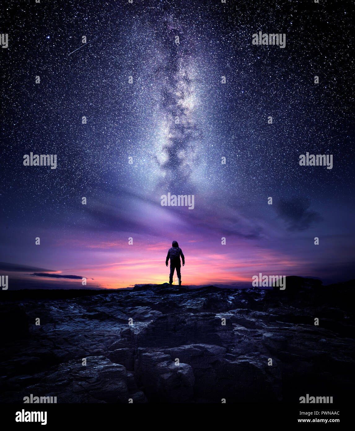 Night time long exposure landscape photography. A man standing in a high place looking up in wonder to the Milky Way galaxy, photo composite. Stock Photo