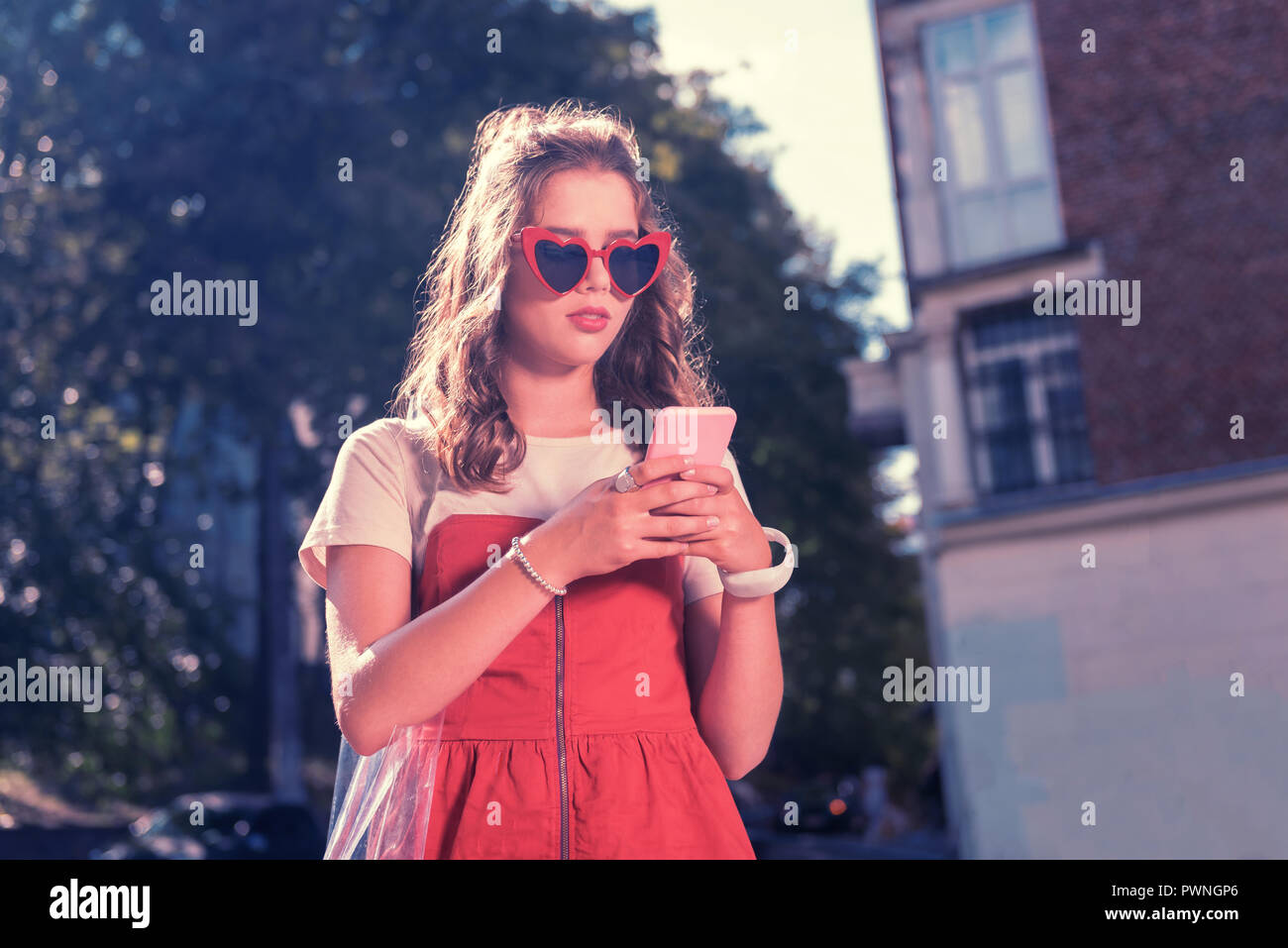 Dark-haired fashionable student holding her pink phone while texting boyfriend Stock Photo