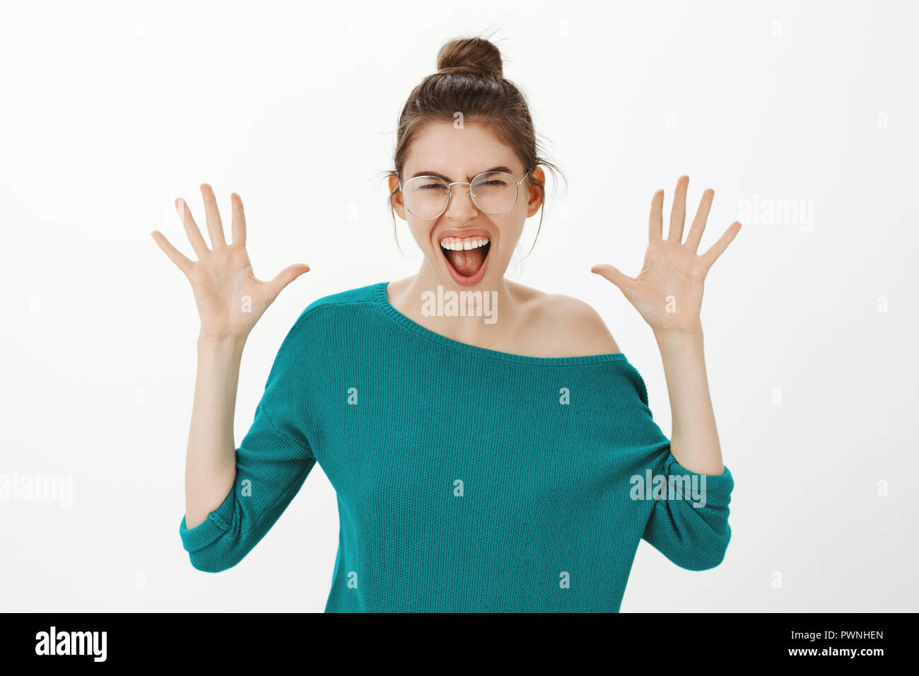 Jazz hands never come out of style. Portrait of joyful carefree caucasian woman in eyewear and loose sweater, shouting or making roar while raising palms and frowning, mimicking lion over grey wall Stock Photo
