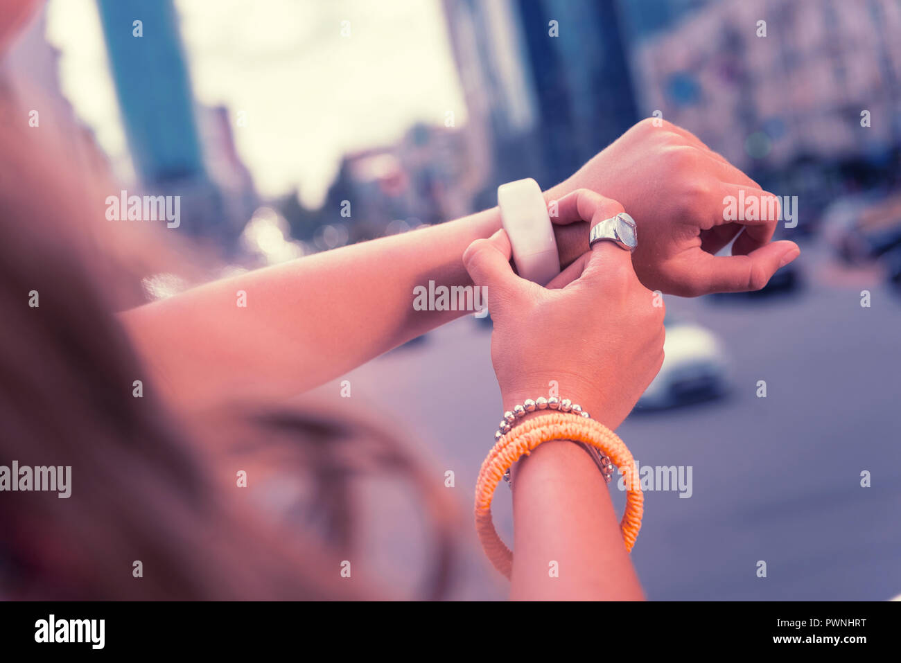 Modern dark-haired girl using her new white smart watch while standing outside Stock Photo