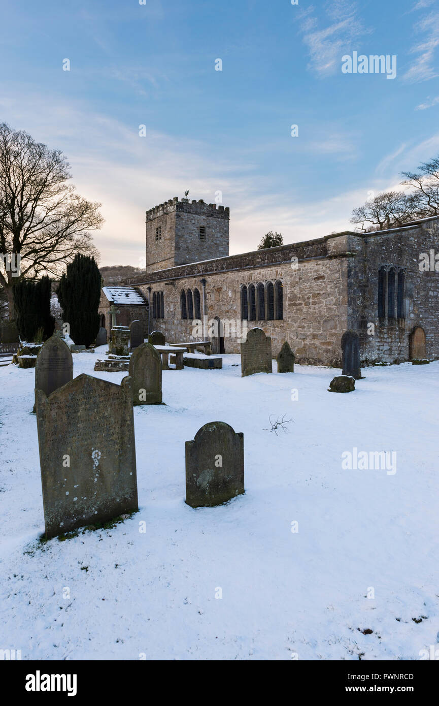 Snowy winter exterior of St Michael and All Angels Church with headstones in snow-covered churchyard - Hubberholme, Yorkshire Dales, England, UK. Stock Photo