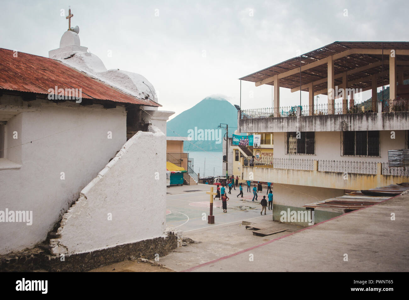 School kids play ball games on a church courtyard in the center of San Juan La Laguna, with views of a volcano and Lake Atitlán, Guatemala Stock Photo