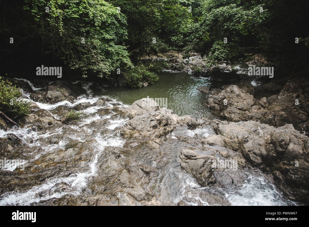 Rocky stream turns into waterfall that feeds a green natural pool in the forest of Montezuma, West coast Costa Rica Stock Photo