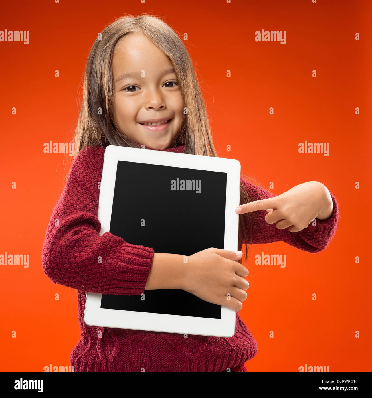 Little funny girl with tablet on studio background. She showing