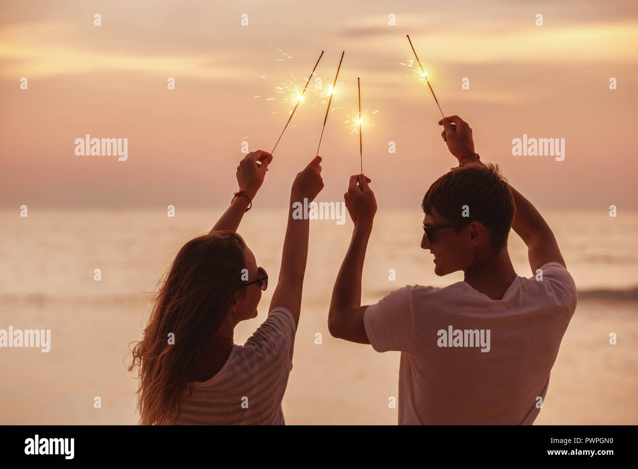 Happy couple having fun and celebrates sunset with sparklers in hands Stock Photo