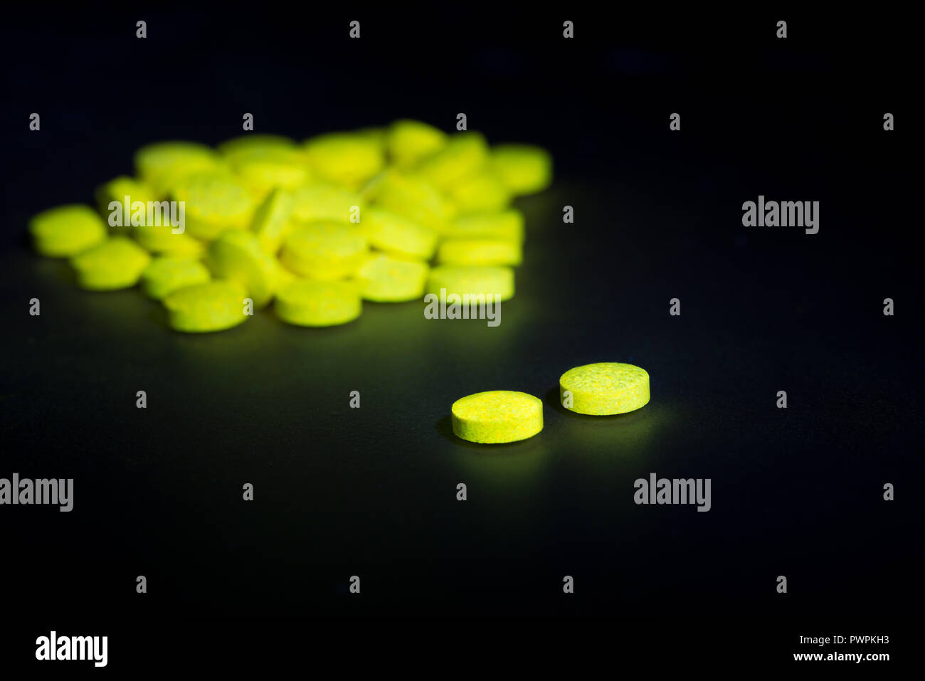 Glowing vitamin B complex pills and tablets fluorescing visible yellow light having been exposed to blacklight, glowing in darkness Stock Photo