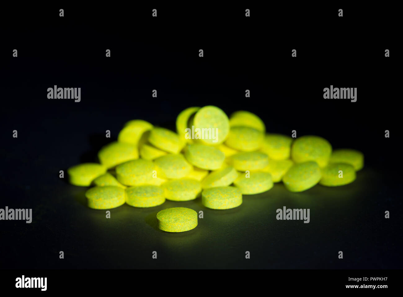 Glowing vitamin B complex pills and tablets fluorescing visible yellow light having been exposed to blacklight, glowing in darkness Stock Photo