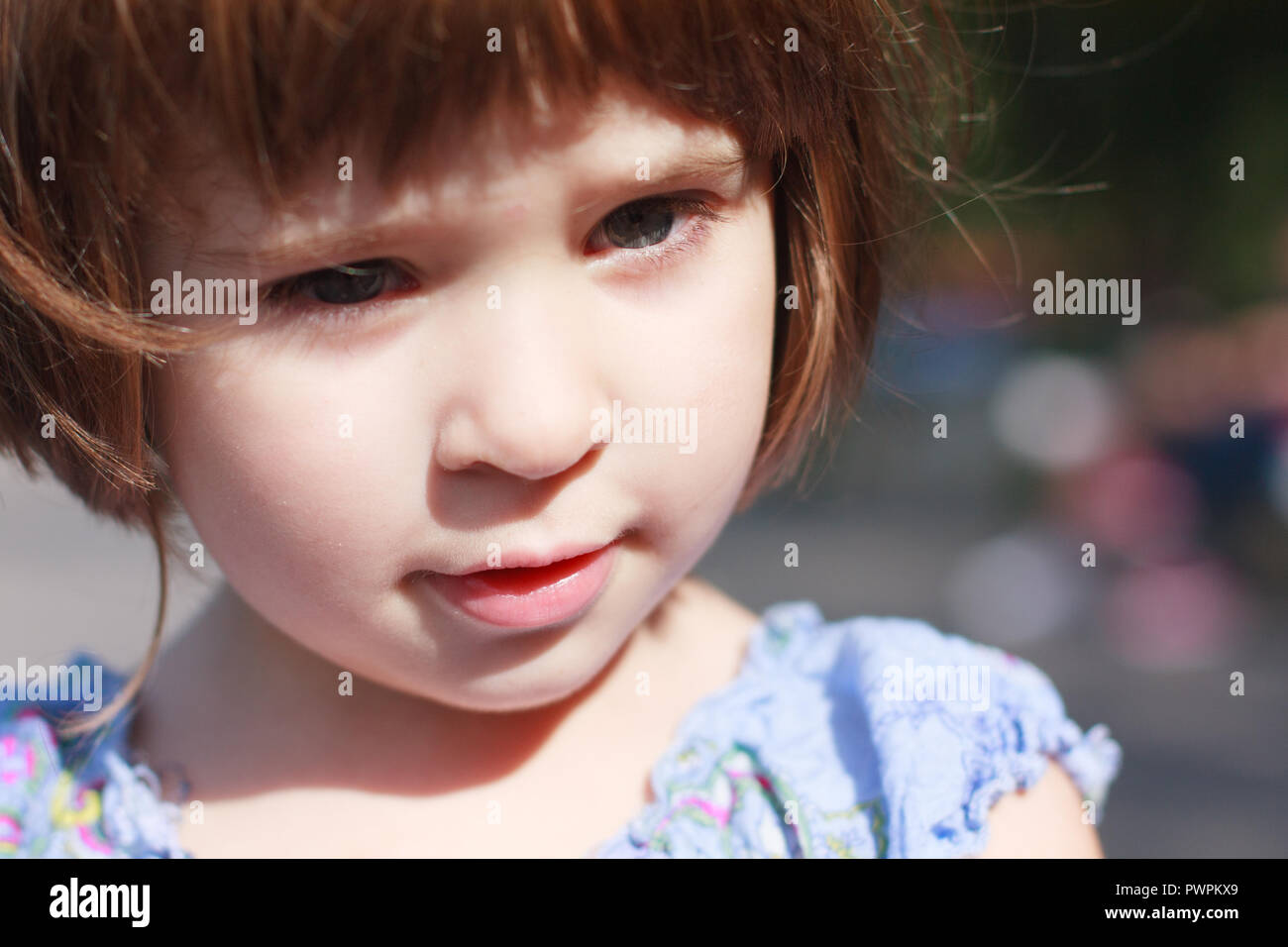 close up portrait of young curious child with short hair, wearing a blue dress Stock Photo