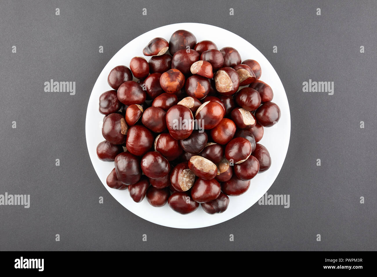 Many chestnuts on white plate. Grey background. Stock Photo