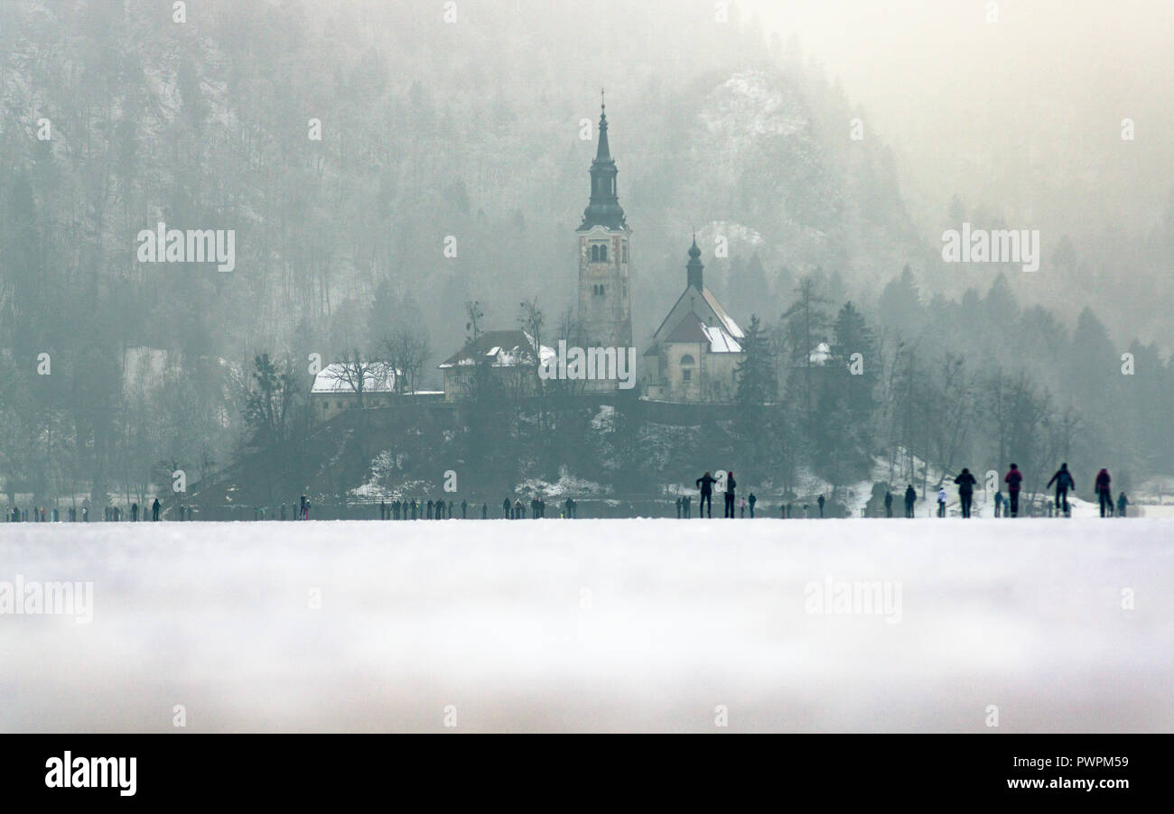 Frozen lake Bled in winter. People walking to the island on thick ice. Stock Photo