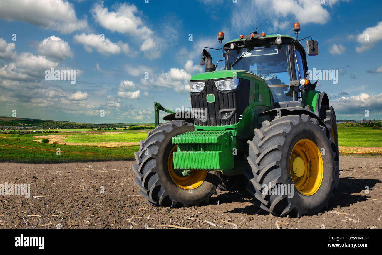 Modern, green tractor in the spring field work on the background of a beautiful rural landscape. Stock Photo
