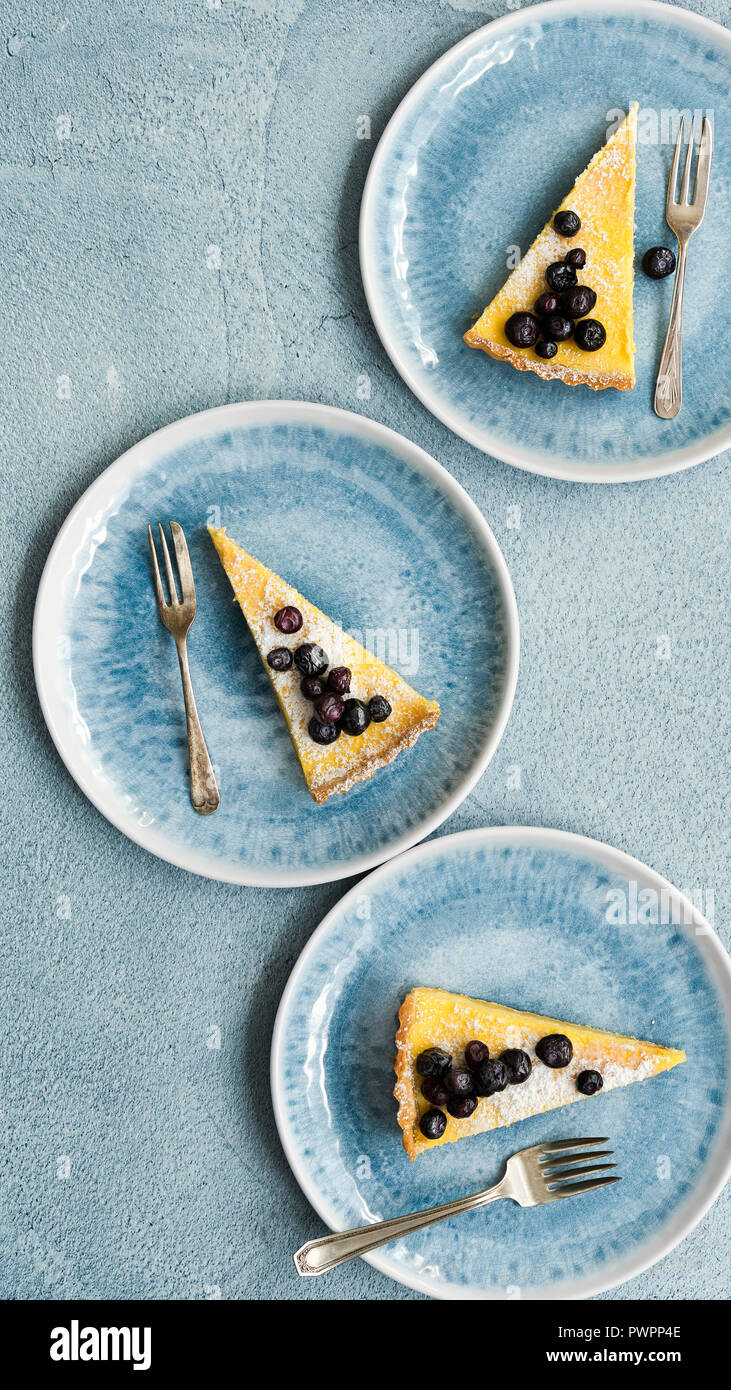 Three slices of lemon and blueberry tart on plates. Stock Photo